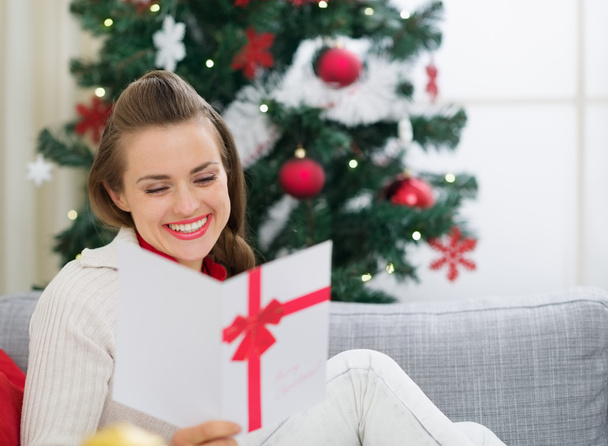 Smiling young woman reading Christmas postcard - 写真・画像