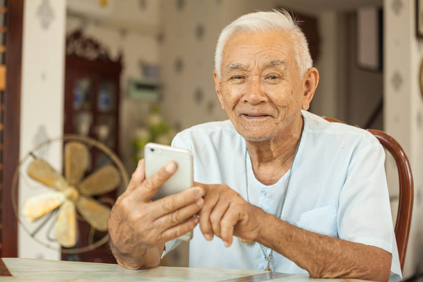 Gelukkig Aziatische senior man met behulp van de mobiele telefoon thuis - Foto, afbeelding