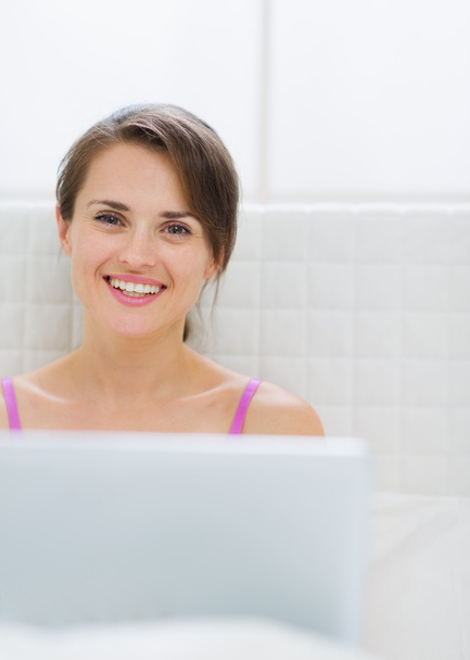 Portrait of happy young woman with laptop in bed - Фото, изображение
