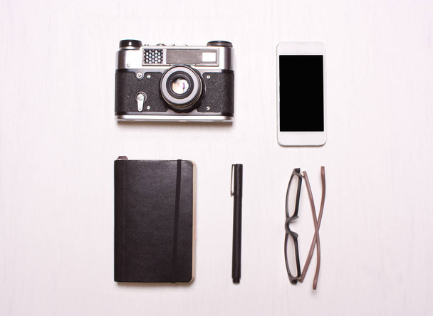 anillos, gafas, cámara, teléfono, cuaderno un fondo blanco
 - Foto, imagen