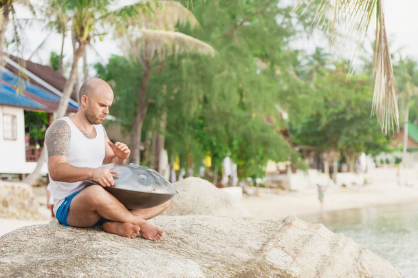 Man is sitting on the stone and playing hangdrum - Foto, Imagem