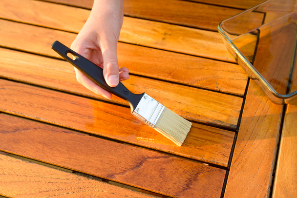 mano sosteniendo un pincel aplicando pintura de barniz sobre una mesa de jardín de madera
 - Foto, imagen