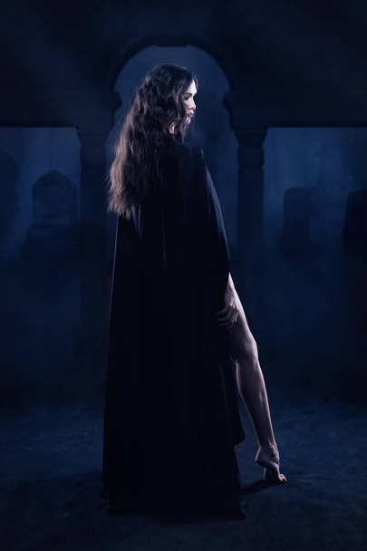 Beautiful gothic girl in a black cloak against a nightscape in t - Fotoğraf, Görsel