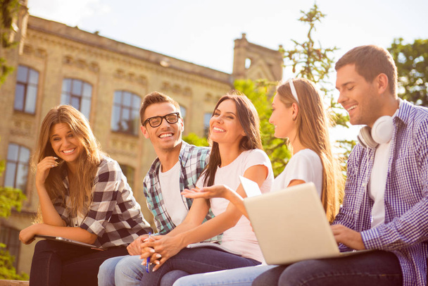 five happy classmates laughing and sitting on bench near college - Foto, Bild