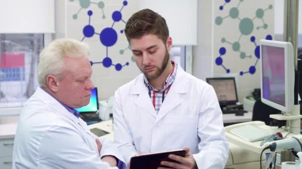 Erkek bilim adamı bir şey onun iş arkadaşınız laboratuvarı için onun tablet üzerinde gösterir - Video, Çekim