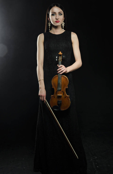 Woman with violin in a black dress standing on black background - Фото, зображення