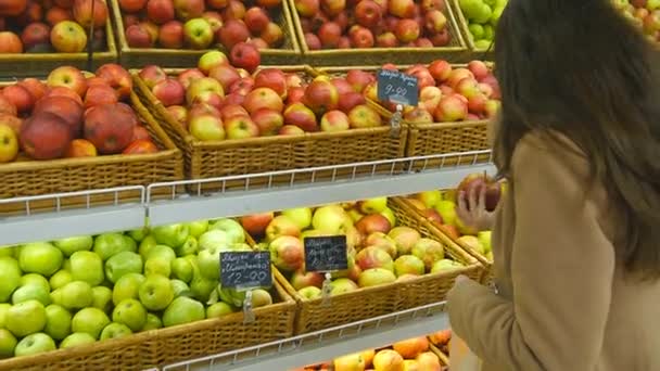 Mujer seleccionando manzanas rojas frescas en el departamento de productos de comestibles y poniéndolo en una bolsa de plástico. Chica bonita joven está eligiendo manzanas en el supermercado y ponerlos en la cesta de la tienda. De cerca.
 - Metraje, vídeo