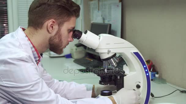 Mies katsoo mikroskoopin läpi laboratoriossa.
 - Materiaali, video