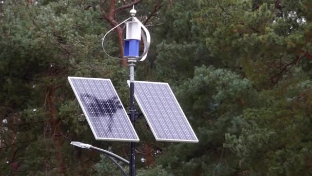 ein sich drehender Wettersensor mit zwei in der Nähe vor dem Waldhintergrund angebrachten Sonnenkollektoren. grüne Energie. - Filmmaterial, Video