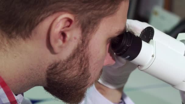 Man looks into the eyepieces of microscope at the laboratory - Materiaali, video