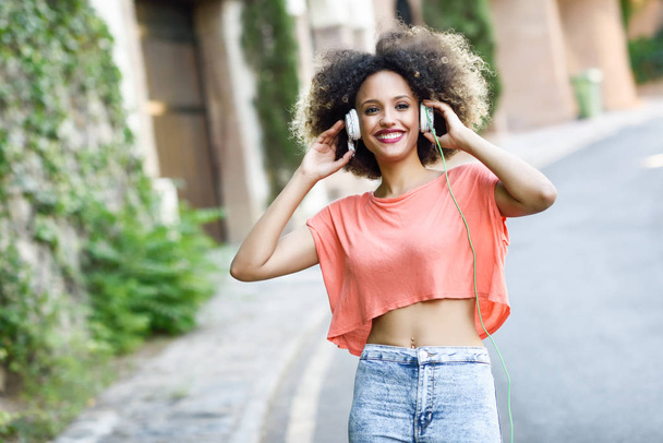 Молода чорна жінка з афро зачіскою посміхається в міському парку
 - Фото, зображення