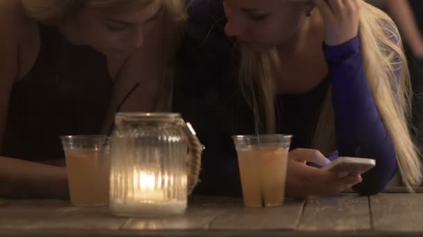 Twee vriendinnen browsen op smartphone zittend in café, vergadering - Video