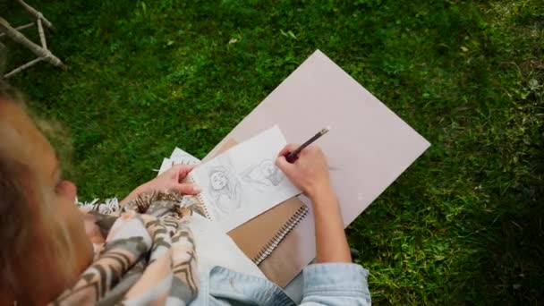 Keze művész lány teszi a nyomtatványok, biztos, hogy éles ceruzával stroke vázlat ismeretlen lány portréja, amely ábrázolja. Mester ül a szabadban Park. - Felvétel, videó