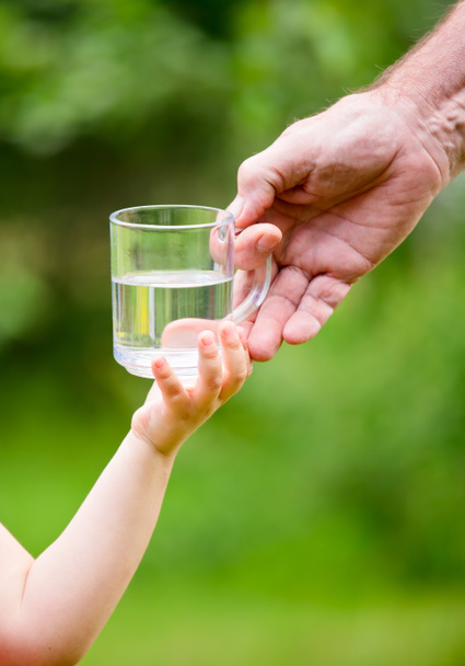 Pieni tyttö ottaa lasillisen vettä isoisältä
 - Valokuva, kuva