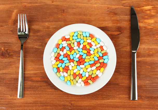 a lot of pills in a plate with knife and fork on wooden background close-up - Fotografie, Obrázek