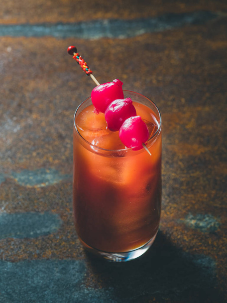 roter Cocktail (blutige Marihuana-Nahaufnahme) in einem glatten Glas mit baumrosa marinierten Zwiebeln darüber, rostiger Hintergrund. vertikales Foto, Seitenlicht - Foto, Bild