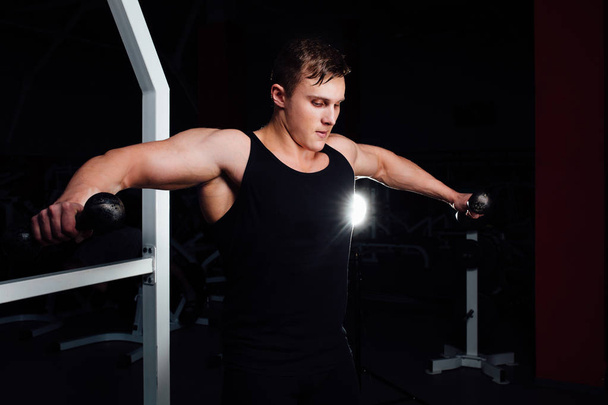 Portrait of a muscular young man lifting weights on gym background. Exercise  the shoulders - Foto, imagen