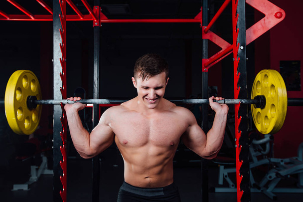 portrait of a handsome athlete at gym. man does the exercise with  barbell, standing and squatting. big confident - Foto, Bild