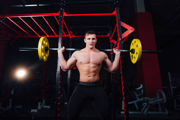 portrait of a handsome athlete at gym. man does the exercise with  barbell, standing and squatting. big confident - Фото, зображення