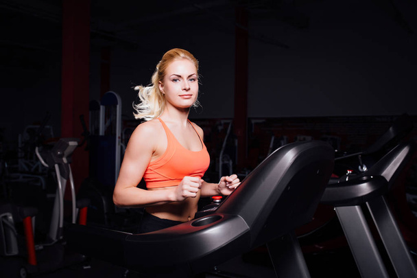 Young beautiful cute girl in fitness model in the gym running on the treadmill with bottle - Foto, imagen