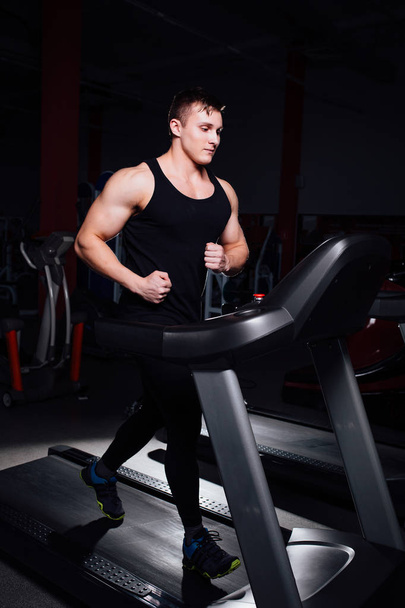 Young strong big man fitness model in the gym running on the treadmill with water bottle. - Foto, Bild