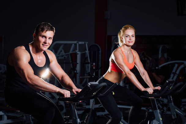 Sporty couple exercising at the fitness the exercise bike on a dark  gym. - Zdjęcie, obraz
