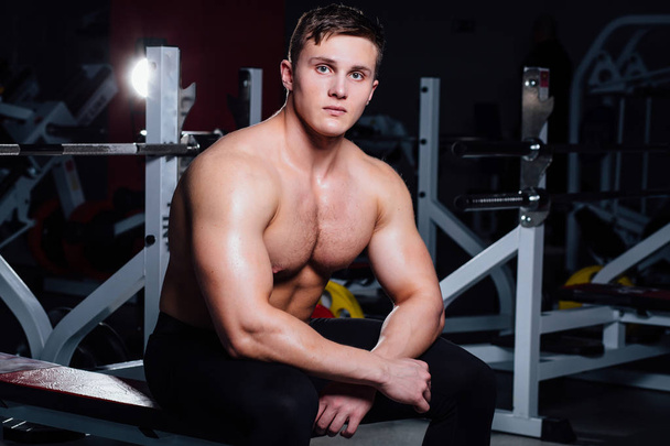 Young handsome man relaxing on barbell bench after workout in gym - Photo, image