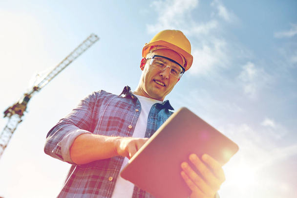 builder in hardhat with tablet pc at construction - Foto, afbeelding