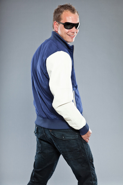 Jovem feliz com cabelo curto usando jaqueta de beisebol azul e jeans azul
. - Foto, Imagem