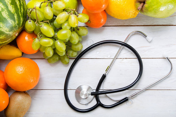 Fruits and stethoscope on white wooden table. - Fotó, kép
