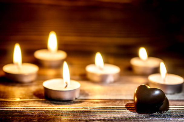 Los corazones de chocolate se encuentran en una superficie de madera. En el fondo se encienden pequeñas velas
. - Foto, imagen