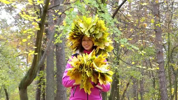 Ευτυχισμένος κορίτσι με το στεφάνι από φύλλα στο κεφάλι της, ρίχνοντας κίτρινο φύλλα σε στον ουρανό πάνω από το κεφάλι. - Πλάνα, βίντεο
