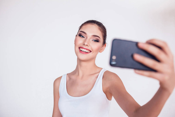 Beautiful brunette girl with makeup make selfie on white background. - 写真・画像