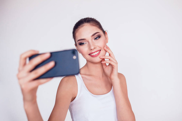 Beautiful brunette girl with makeup make selfie on white background. - 写真・画像