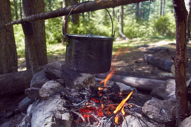 Cauldron boils on the fire in the forest. In marching a saucepan preparing food. Adventure tourism, camping, cooking on a fire. Survival in the forest. Stalker - 写真・画像