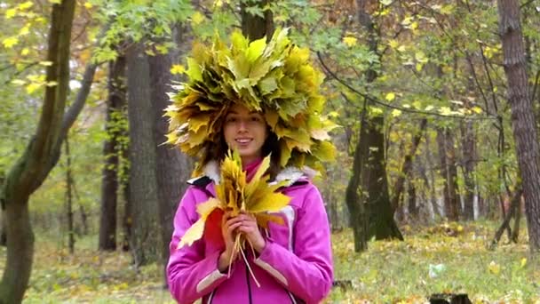 Χαμογελαστό κορίτσι με στεφάνι από φύλλα στο κεφάλι στο δάσος. - Πλάνα, βίντεο