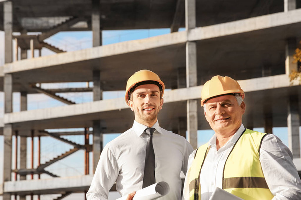 Handsome engineer and worker standing against unfinished building - Photo, image