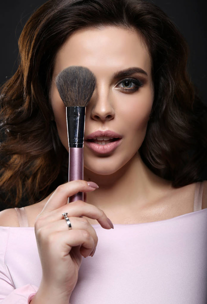 gorgeous woman with dark hair finishing her makeup using powder  - Фото, изображение