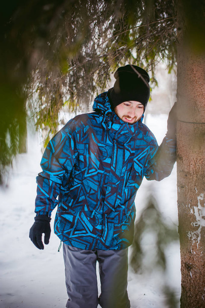 men walk in a winter park. guy with good humor and smile, warm clothing walking outdoors, looking out of coniferous trees - Foto, imagen