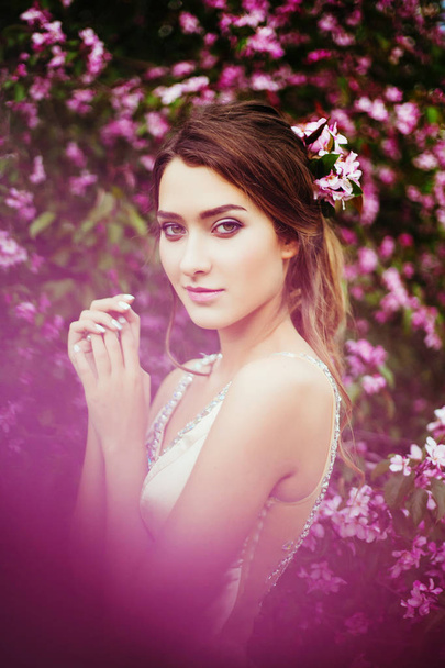 Portrait of young beautiful woman posing among blooming apple trees. - Foto, afbeelding