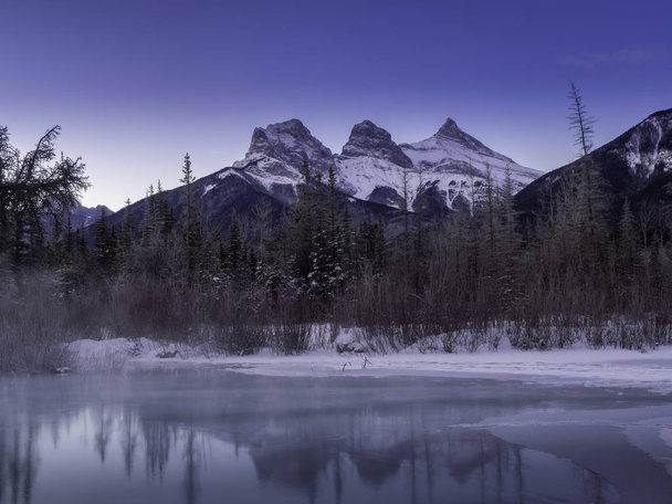 Vista del amanecer de las Tres Hermanas desde un arroyo congelado de policías a lo largo del río Bow en las afueras de Canmore, Alberta en invierno
. - Foto, imagen