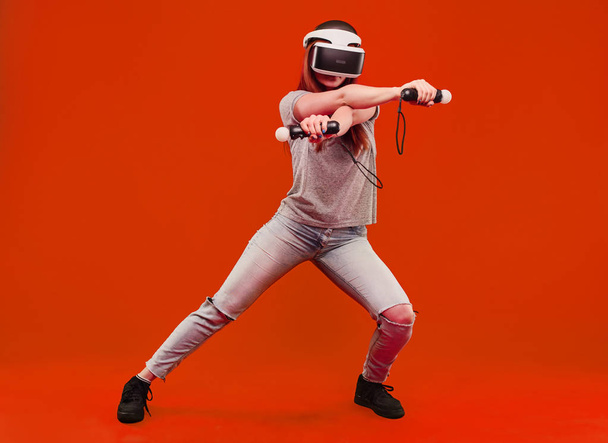 happy young woman in virtual reality helmet isolated on orange background jumping and smiling. VR glasses. - Photo, Image