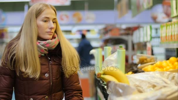 Mujer tomando un plátano en una tienda de comestibles con frutas y verduras
 - Metraje, vídeo