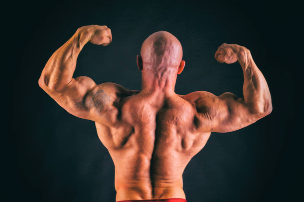 Bodybuilder posant dans différentes poses démontrant leurs muscles. Échec sur fond sombre. Homme montrant des muscles tendus. Magnifique athlète du corps musculaire
. - Photo, image