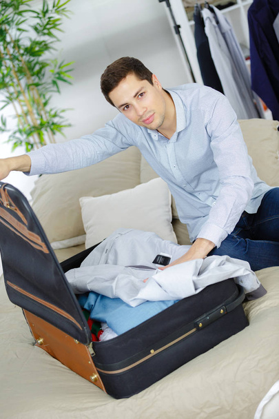 young man unpacking suitcase in hotel room - Foto, Bild