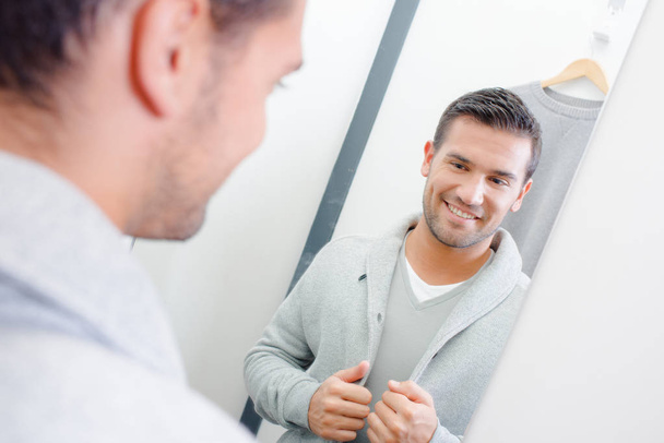 Man trying on jacket, looking at reflection in mirror - Photo, image
