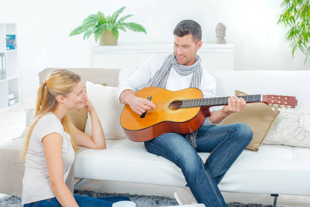 Man on couch, playing guitar to lady - Φωτογραφία, εικόνα