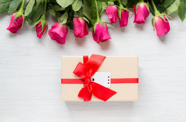 Pink rose en cadeau met rood lint op witte houten achtergrond - Foto, afbeelding
