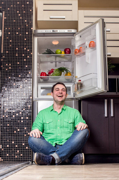 Young Man Sitting In Front Of Fridge - Foto, imagen