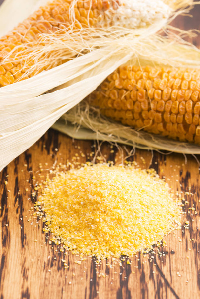 Кукурузная крупа и семена, кукурузные початки на деревянном деревенском столе
 - Фото, изображение